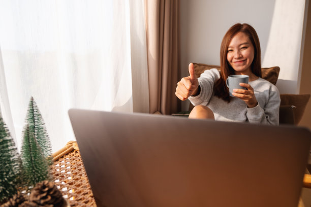 一位年轻美丽的亚洲女子在家里用笔记本电脑进行视频通话时竖起大拇指图片下载