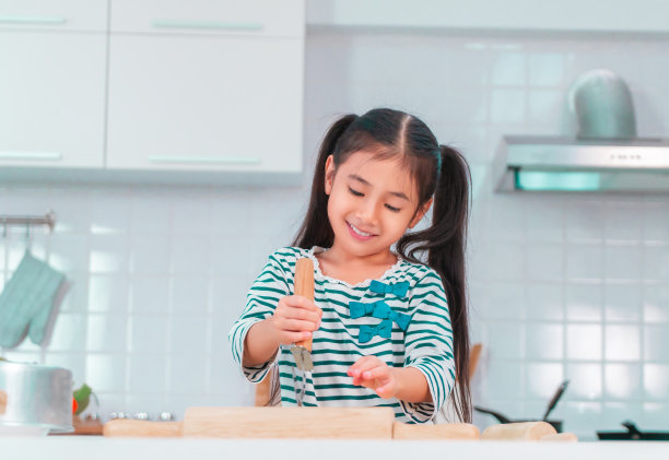 快乐的亚洲女孩有乐趣准备披萨面团在厨房和微笑有趣的儿童活动概念。图片下载