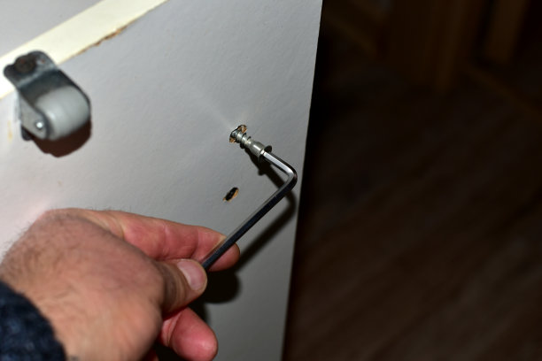 他手里拿着一把六角钥匙，用它从家具的侧面拧下一颗螺丝钉。图片下载