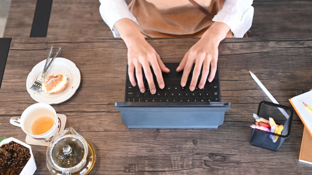 头顶上的照片，年轻的自由职业女性在木桌上用电脑平板电脑工作，吃着早餐。图片下载