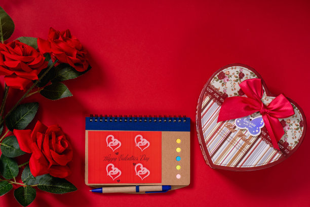 红色玫瑰和心形盒子，红色背景上有记事本和钢笔。复制space-stock照片图片下载