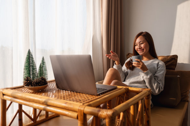 一位年轻的亚洲女子坐在家里喝着咖啡，用笔记本电脑进行视频通话图片下载