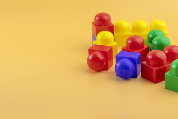 在黄色背景上建造玩具塑料人物和砖块。彩色塑料砖。图片下载