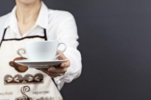 喝咖啡的时间。一个咖啡师拿着并呈现一杯热咖啡孤立在一个黑色的背景。图片下载