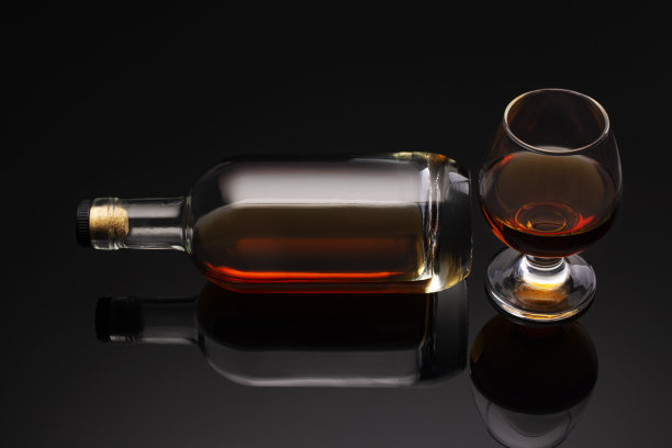 深色背景上的一瓶白兰地和一只玻璃杯。图片下载