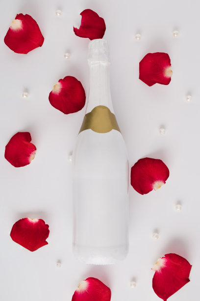 搭配一瓶香槟、玫瑰花瓣和珍珠的创意组合。最小的爱的概念。母亲节或情人节的想法。图片下载