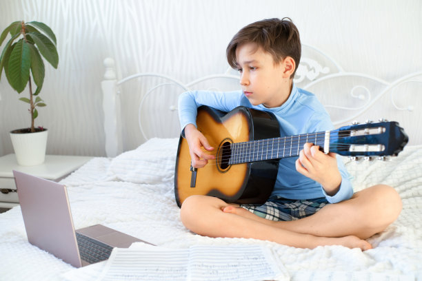 男孩正在网上学习用笔记本电脑弹吉他图片下载