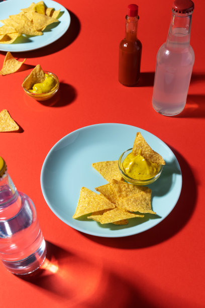 蓝色的盘子上有奶酪酱的玉米片，苏打水瓶和红底的辣椒酱。食物的照片,垂直图片下载