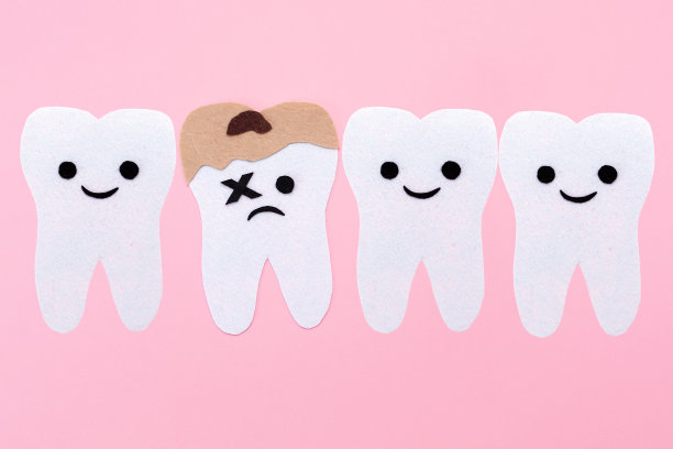 用毛毡雕刻的一排牙齿和卡通面孔。有一颗牙齿有蛀牙。粉红色的背景。副本的空间。口腔医学和口腔卫生的概念图片下载