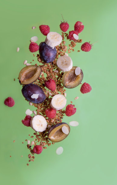 落下来的麦片，覆盆子，李子，香蕉在绿色的背景上。食物悬浮图片下载