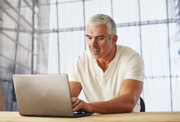 白人商人在工作场所穿着休闲衬衫使用笔记本电脑的肖像图片下载