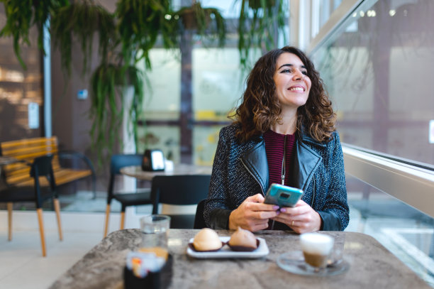 女人坐在咖啡馆里用智能手机喝着咖啡吃着糕点。图片下载