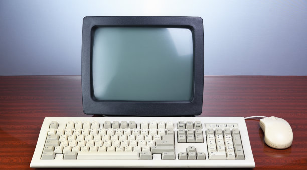 一张棕色的老式桌子上放着一台老式的CRT显示器，上面有1990年的键盘。旧复古的电脑。图片下载