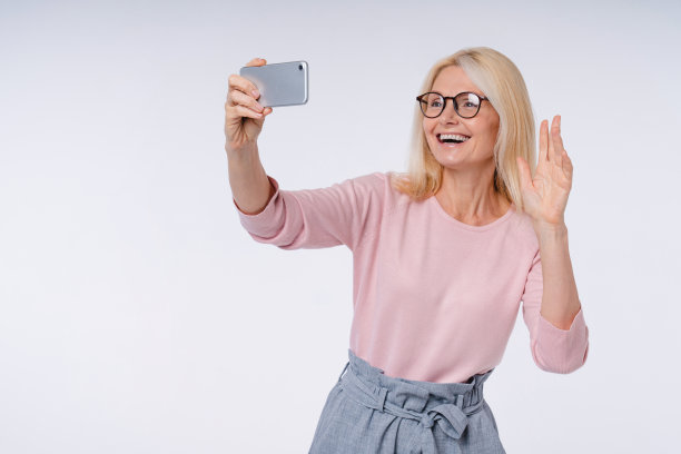 中年美丽的女人在网上聊天用她的手机孤立在灰色的背景图片下载