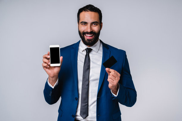 手持信用卡和手机的成功年轻中东男商人，灰色背景图片下载