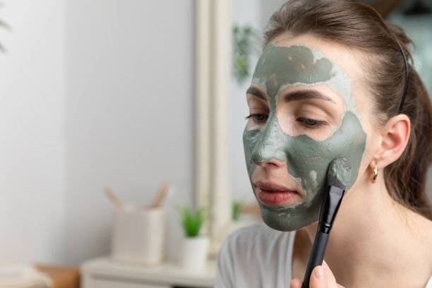 一个美丽的女人用绿色粘土面膜的特写。用刷子触碰她的皮肤。美容护肤理念。图片下载