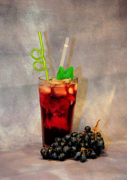 在灰色的背景上，摆着一串红葡萄和一杯带冰的鲜亮花蜜。图片下载