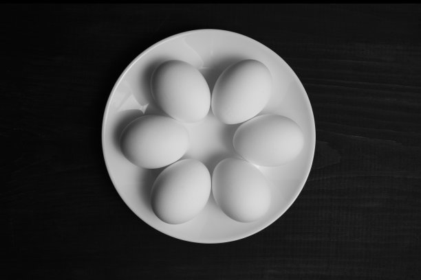 鸡蛋放在光滑的白色盘子里。白色的盘子上有鸡蛋，背景是黑色的木头。图片下载