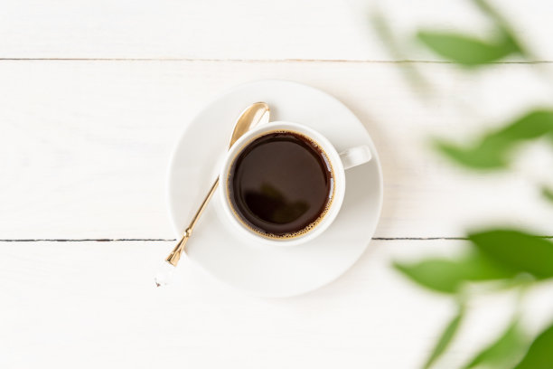 白色木桌和绿色树叶上的咖啡俯视图。早上的能量饮料。素材图片
