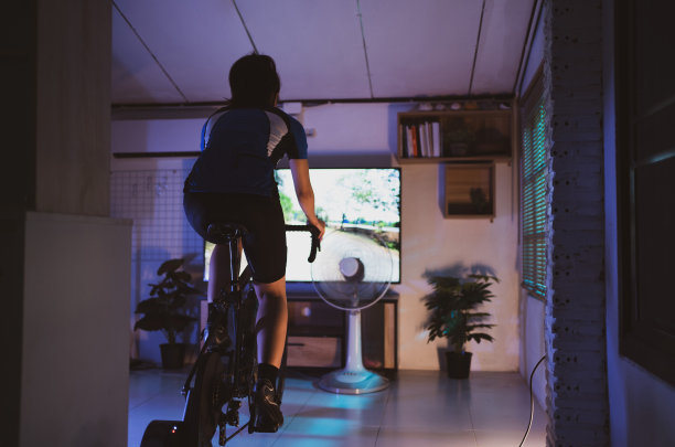 亚洲女人骑自行车。她在家锻炼。晚上她在虚拟世界里玩游戏。图片下载