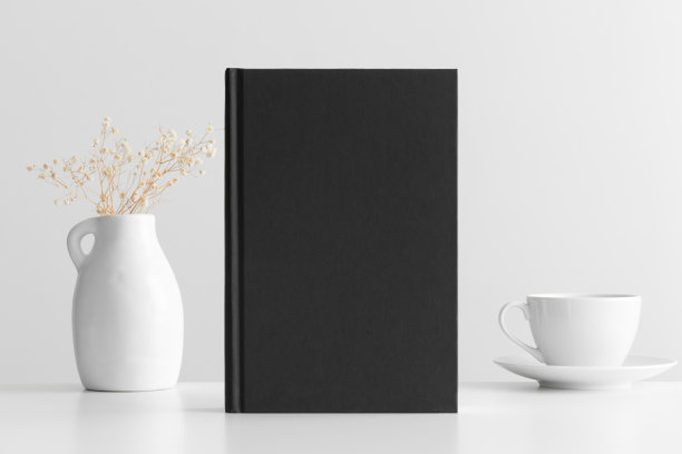 白色桌子上放着一杯咖啡，装饰着吉普赛菲拉的黑书模型。图片下载