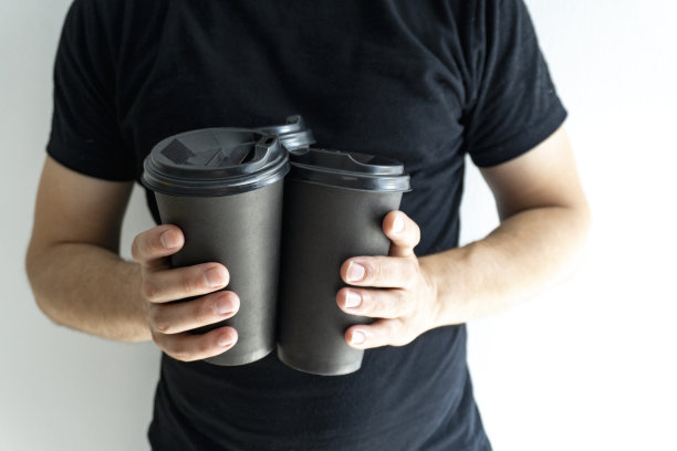 特写在白人男子的手与三个togo咖啡在黑色纸杯黑色盖子，没有脸，只有手，没有持有人，特写，外卖咖啡概念，黑色t-short和白色背景，复制空间。图片下载