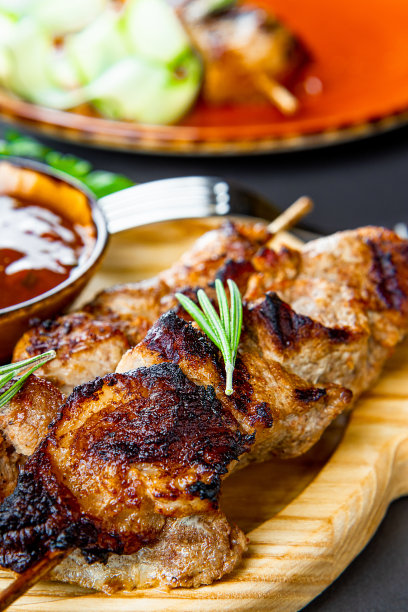 烤猪肉串与黄瓜沙拉和烧烤酱在切板上近距离垂直照片图片下载