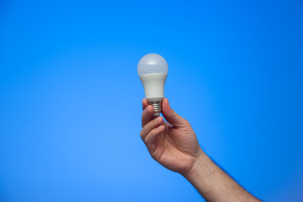 白种人男性的手拿着一个白色不透明的灯泡近距离隔离在蓝色背景的工作室拍摄图片下载