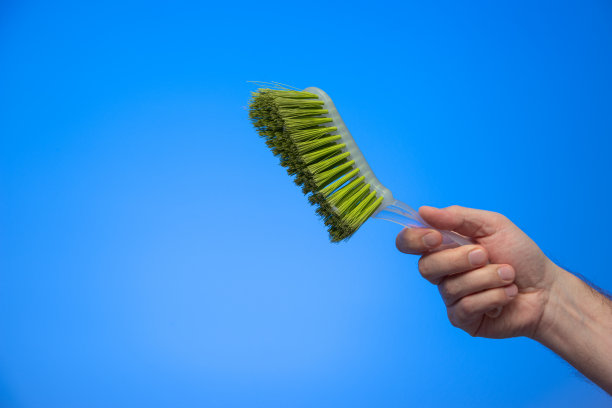 白种人男性手握绿色塑料扫地刷孤立在蓝色背景工作室拍摄图片下载