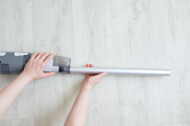 白人妇女的手把金属管灰色吸尘器放在白色的木质背景上。图片下载
