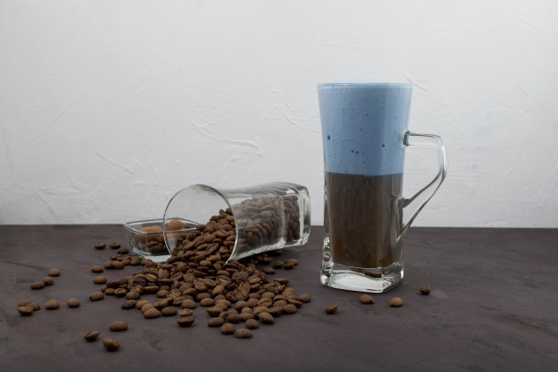 卡布奇诺或拿铁咖啡与蓝色牛奶泡沫在高脚杯。烘好的咖啡豆撒在桌子上。选择性聚焦，复制空间图片下载