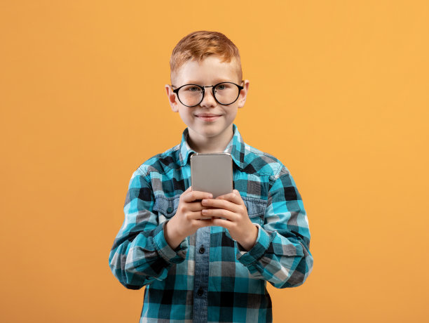 微笑的男生在手机上玩游戏，黄色的背景图片下载