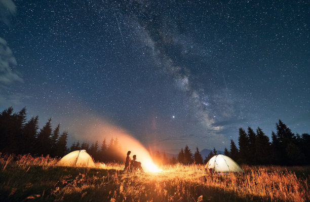 在美丽的星空下，一对年轻的夫妇坐在篝火旁。图片下载