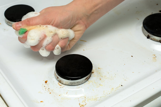 在一个女人的手里，一块海绵泡沫，清洁一个肮脏的炉子。这个想法就是做家务，保持清洁。横向照片，大计划。图片下载