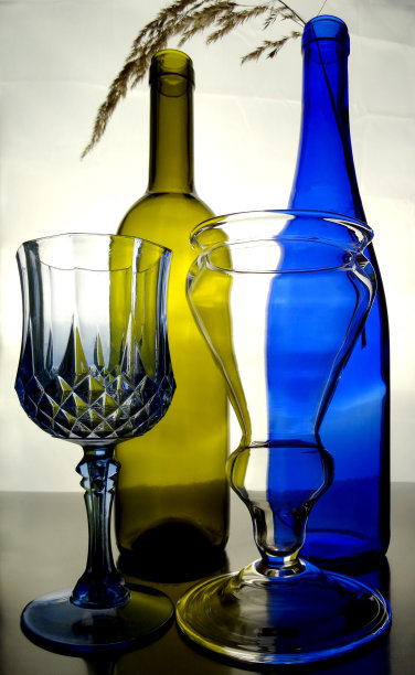 瓶子和葡萄酒杯由彩色玻璃制成，在一个明亮的背景图片下载