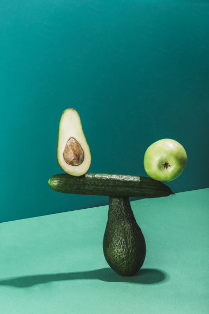 平衡新鲜蔬菜和水果的概念，黄瓜，鳄梨和在绿色背景下的苹果。图片下载