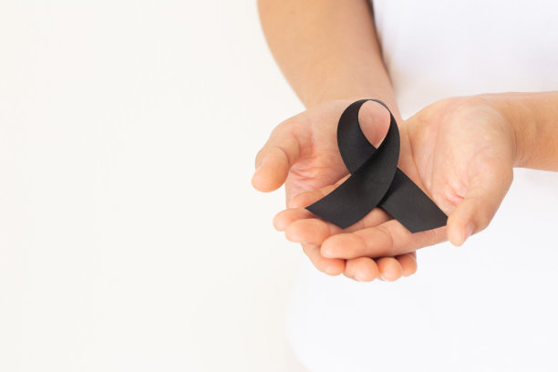 手握黑色丝带在白色背景与复制空间，象征皮肤癌意识月五月，黑素瘤癌症，悼念丝带象征。医疗保健和保险概念。图片下载