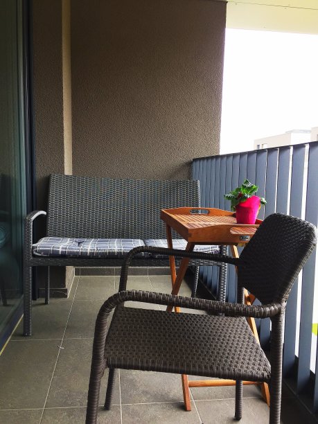 阳台上有一把扶手椅、一个带枕头的沙发和一张桌子。图片下载