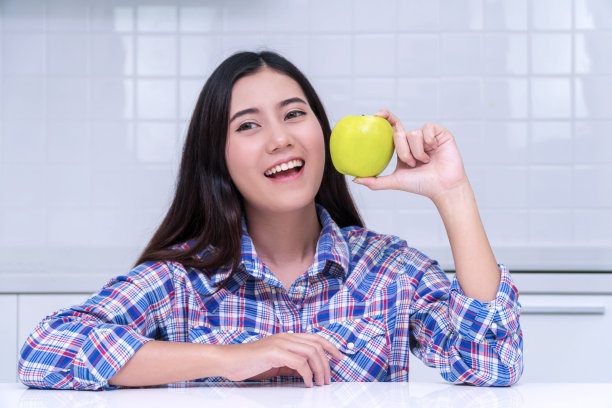 健康饮食的概念。笑容满面的年轻女子拿着新鲜的绿苹果，在厨房的镜头上用早餐盖住了她的脸。图片下载