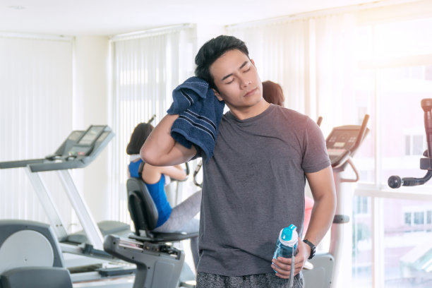 年轻男子运动员擦拭他的喉咙与蓝色毛巾颈部锻炼后，而在他的手拿着水与拷贝空间。概念运动与健康。图片下载