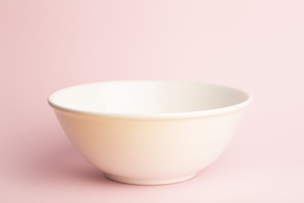 粉色背景上的白色碗。一个干净的粉红色背景上的大空陶瓷碗。图片下载