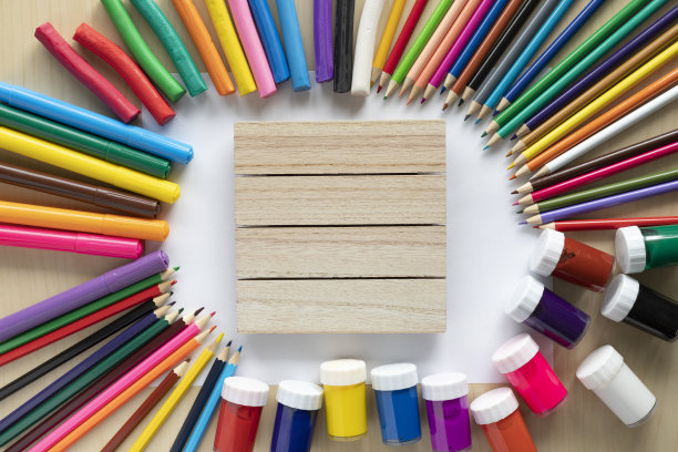 平铺的彩色颜料、马克笔、铅笔和橡皮泥在桌子上，中间是木制的招牌图片下载