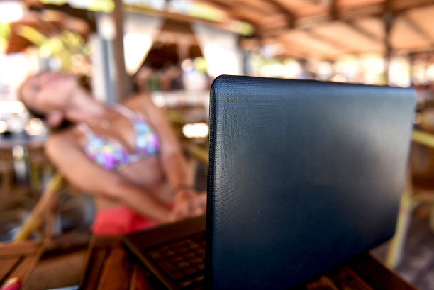 一个女人穿着泳衣在海滩酒吧工作在她的笔记本电脑作为一个自由职业者库存照片图片下载