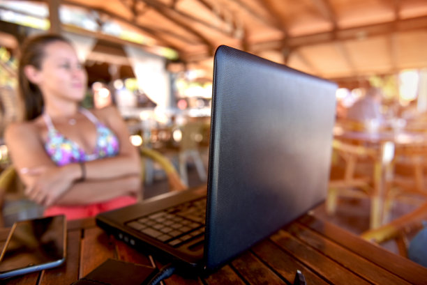 一个女人穿着泳衣在海滩酒吧工作在她的笔记本电脑作为一个自由职业者库存照片图片下载