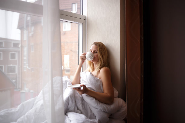 一个裹着毯子的女人坐在大窗户旁边的窗台上图片下载