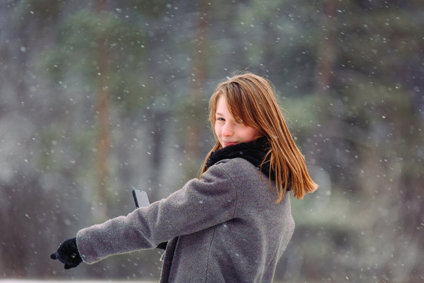 女孩用食指指着旁边，用手机拍下了小雪花的背景。图片下载