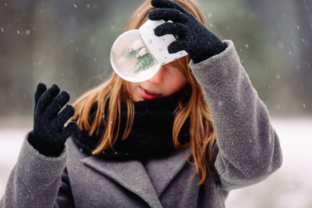 一个漂亮的女孩惊讶地摇着她面前的玻璃雪球。放大照片魔幻的一面在冬天魔法背景与小雪花。图片下载