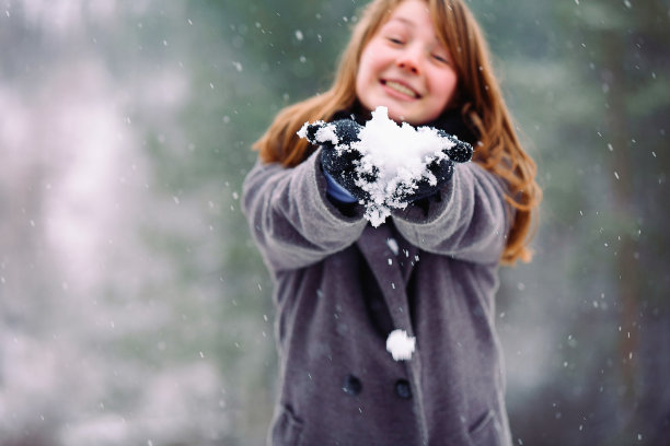 一张模糊的照片，一个红鼻子的年轻女孩手里拿着一个雪球。冬季森林和消遣。图片下载