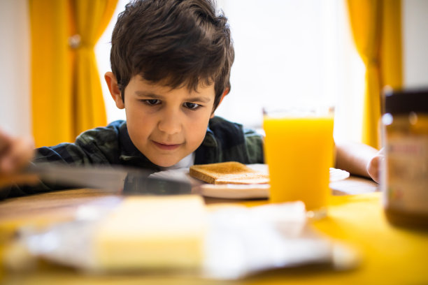 一个可爱的男孩在吃早餐时专注于用刀切黄油图片下载