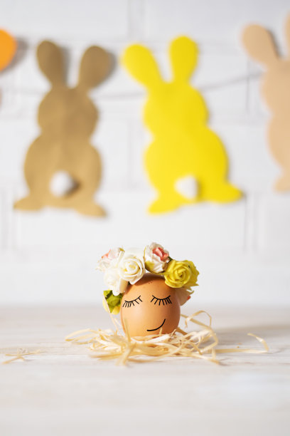 复活节彩蛋和滑稽的脸。有趣的复活节彩蛋装饰黄玫瑰花环和纸兔子。复活节彩蛋正在睡觉。图片下载